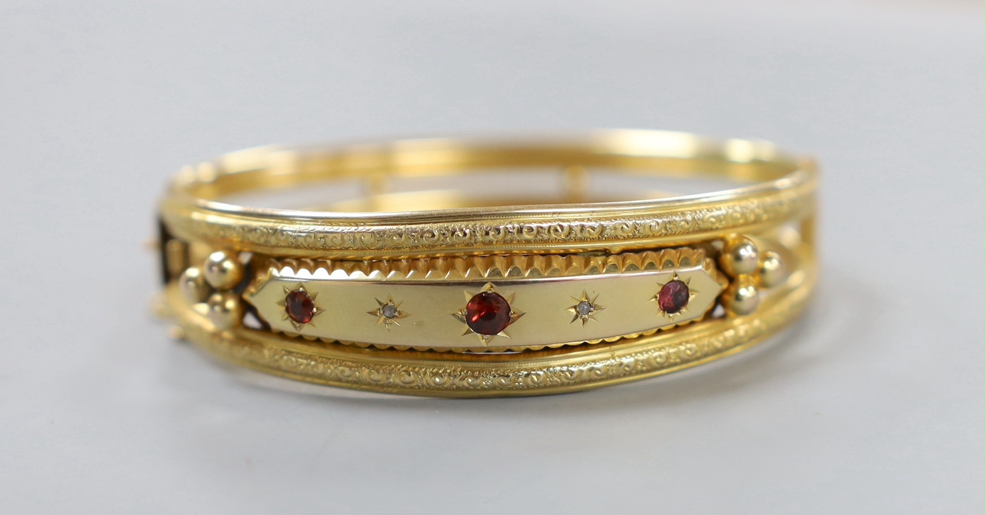An Edwardian 9ct gold and three stone garnet and two stone diamond chip set hinged bangle, gross weight 12.5 grams.